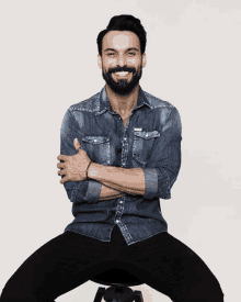 a man with a beard is sitting on a chair with his arms crossed .