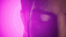 a close up of a woman 's face with purple lighting behind her .