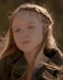 a young girl with a braided headband is looking at the camera