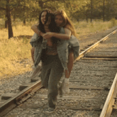 a woman is carrying another woman on her shoulders on train tracks