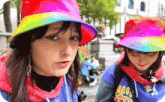 a woman wearing a rainbow hat is standing next to another woman wearing a blue shirt that says ' noodles '
