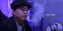 a man wearing a hat and smoking a cigarette with the word paling dingin in the corner