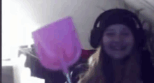 a woman wearing headphones and a hat is smiling while holding a pink balloon .