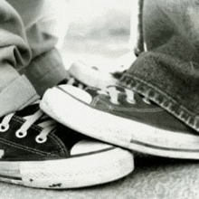 a black and white photo of a person 's feet wearing converse sneakers .