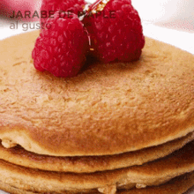 a close up of a stack of pancakes with raspberries on top and the words " jarabe de arce al gusto " on the bottom