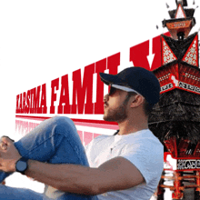 a man sits in front of a sign that says karsima fami