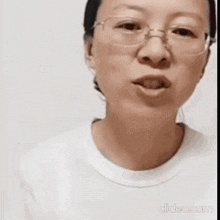 a woman wearing glasses and a white shirt is making a face with her eyes closed .