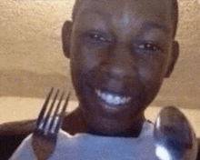 a man is smiling while holding a fork and spoon in front of his mouth .