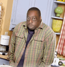 a man wearing a plaid shirt is standing in a kitchen