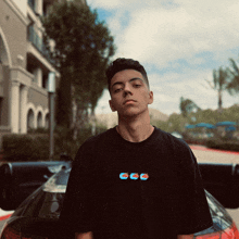 a young man wearing a black t-shirt that says ccc stands in front of a black car