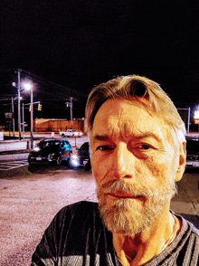 a man with a beard is taking a selfie in a parking lot at night