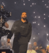 a man in a black jumpsuit is walking on a stage surrounded by phones