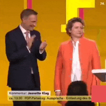 a man and a woman are standing next to each other on a stage . the woman is wearing an orange jacket .