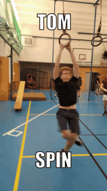 a man is hanging from a rope in a gym with the words tom spin above him