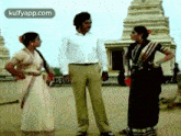 a man and two women are standing next to each other on a dirt road in front of a building .