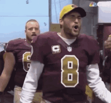 a football player in a maroon jersey with the number 8 on it is standing in a locker room .