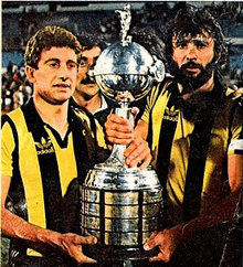 a man in a yellow and black adidas shirt holds a large trophy