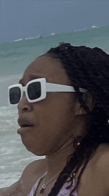 a woman wearing white sunglasses is making a funny face on the beach