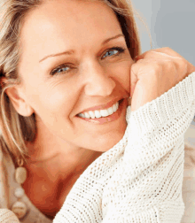 a woman wearing a white sweater is smiling with her hand on her chin