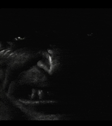 a close up of a man 's face in the dark with his mouth open and teeth showing .