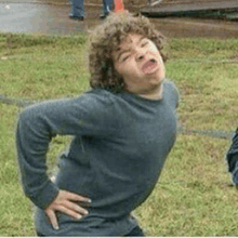 a young man with curly hair is making a funny face while standing in a grassy field .