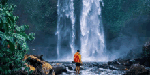 a man with a backpack standing in front of a waterfall .