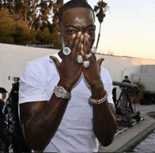 a man wearing rings and a watch covering his face with his hands