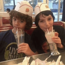 two young boys are drinking milkshakes in a diner and one has a shirt that says live out