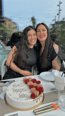 two women posing for a picture in front of a birthday cake