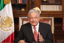 a man in a suit and tie is sitting at a desk in front of a mexican flag