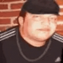 a close up of a man wearing a hat and a necklace in front of a brick wall .