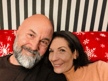 a bald man and a woman are posing for a picture on a red blanket with snowflakes on it