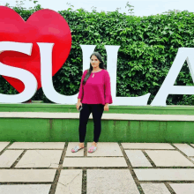 a woman in a pink top stands in front of a sign that says sula