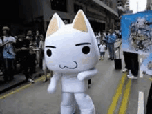 a white cat mascot is walking down a street .