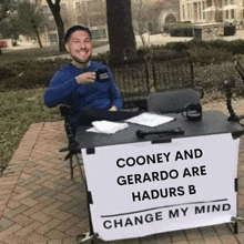 a man sitting at a table with a sign that says ' change my mind '