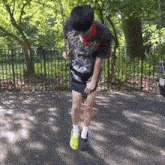 a man wearing a black shirt and yellow crocs is standing in front of a fence in a park .