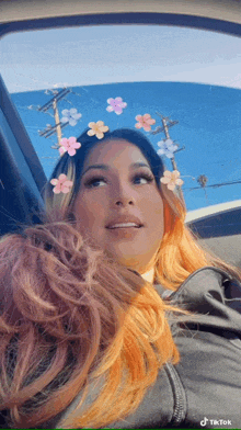 a woman with orange hair is sitting in a car with flowers on her hair .