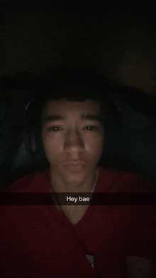 a young man wearing headphones and a red shirt has a snap that says hey bae on it