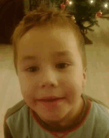 a young boy is smiling in front of a christmas tree and making a funny face .