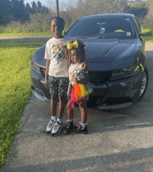 a boy and a girl are posing in front of a black car