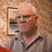 an older man wearing glasses and a striped shirt is standing in front of a framed picture of a body of water .