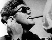 a man wearing sunglasses smoking a cigar while talking on a phone