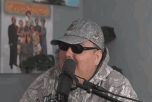 a man wearing sunglasses and a hat is standing in front of a microphone and smiling