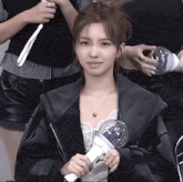 a woman in a black jacket holds a light stick