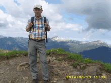 a man in a plaid shirt stands on top of a rocky hill with mountains in the background and the date 2014/06/13