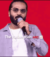 a man with a beard and sunglasses is singing into a microphone with the words the redemption arc behind him