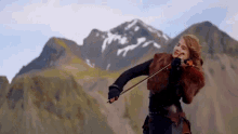 a woman is playing a violin in front of mountains .