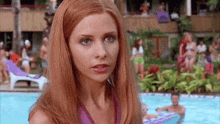 a woman with red hair is standing in front of a pool .