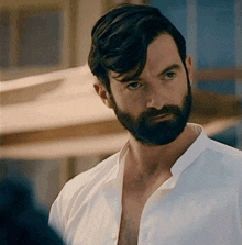 a man with a beard wearing a white shirt looks to the side