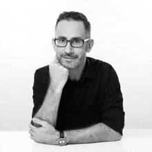 a man wearing glasses and a watch is sitting at a table